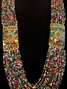 This is a wonderful colorful vintage Naga necklace with two mosaic inlay brass medallions that also serve as connectors for the multi bead strands.  There are 21 strands connected to the top of the mosaic medallion, and 24 rows connected to the bottom of the medallions.   The medallions have a decorative brass sun at center, with their rays having scalloped edges, and a tiny beaded effect frames the center brass circle. The inner circumference of the necklace measures approximately 31". Fastens with a blue disc bead and loop.  Medallions measure approximately 2-1/4" X 1-3/8" Excellent vintage condition.  No issues. Includes gift box and storage pouch. Box 1 Handmade Multicolor Jewelry For Rituals, Traditional Multicolor Medallion Beaded Necklaces, Traditional Multicolor Medallion Beaded Necklace, Traditional Medallion Beaded Necklaces In Multicolor, Bohemian Multicolor Brass Necklace, Bohemian Multicolor Brass Necklaces, Traditional Brass Beaded Necklace With Gold Beads, Multicolor Beaded Jewelry For Rituals, Multicolor Artisan Beads For Festival