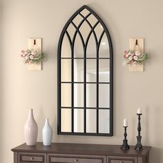 an arched mirror on the wall above a dresser with two vases and a candle holder