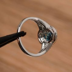 It is a London blue topaz ring. The main stone is 6mm*8mm oval cut, weight about 1.47 carats. The basic metal is sterling silver and plated with rhodium. To change the metal to a solid gold (white/rose) or platinum is also available, please ask for a quotation if you want. You can also go to my shop Home for more elegant rings: https://www.etsy.com/shop/godjewelry?ref=hdr_shop_menu More London blue topaz rings: https://www.etsy.com/shop/godjewelry?ref=seller-platform-mcnav&section_id=2071503 Blue Topaz Rings With Halo Setting, Silver Diamond Ring With Blue Topaz And Halo Setting, Blue Topaz Diamond Ring With Brilliant Cut For Promise, Blue Topaz Rings With Halo Setting In Round Cut, Promise Ring With Bezel Set Blue Topaz, Blue Topaz Cluster Ring For Promise, Topaz Open Ring With Bezel Setting For Anniversary, Topaz Ring With Center Stone, Silver Rings With Halo Setting And Blue Topaz