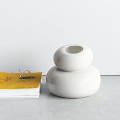 a white vase sitting on top of a table next to a stack of books and a yellow postcard