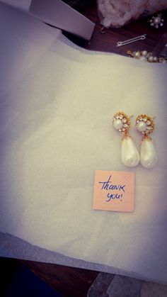 a pair of earrings sitting on top of a piece of paper next to a note