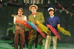 three men are standing on stage with colorful streamers in their hands and one man is wearing a hat