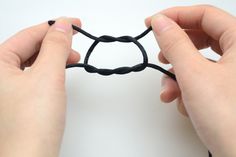 two hands are holding a piece of black string