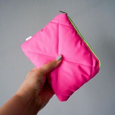 a hand holding a pink pouch with a green zipper