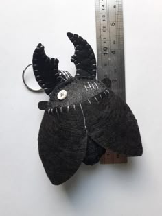 a black stuffed animal hanging from a measuring tape on top of a white table next to a ruler