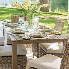 a dining table set with place settings and flowers in vase on the top, outside