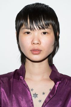 a woman with black hair wearing a purple shirt and star tattoos on her chest is looking at the camera