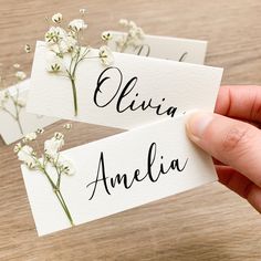 someone holding up two place cards with flowers on them that read, eliivia and amelie