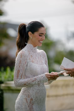 a woman in a white dress smiles as she holds an envelope and looks at it