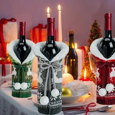 three wine bottles wrapped in christmas sweaters on a table with candles and other holiday decorations