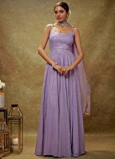 Embrace timeless elegance with the Lavender and Gold Sequin Embroidered Anarkali Gown, expertly crafted from luxurious viscose georgette. This lavender gown is adorned with intricate sequin and threadwork embroidery, bringing a touch of opulence to its design. The flattering strappy round neckline and chic back cutout at the waist introduce a modern flair to the traditional silhouette. Its flowy, floor-length design exudes regal charm, perfectly complemented by the matching net dupatta with delicately embroidered scallop lace. Ideal for Mehndi, Sangeet, or as wedding guest attire, this ensemble seamlessly blends classic allure with contemporary sophistication Composition : Anarkali - Viscose Georgette and Dupatta - Soft net Care: Dry Clean Only and Vacuum Storage This product can be custom Festive Sequined Maxi Dress For Reception, Long Sequined Gown For Festive Occasions, Festive Long Dress Gown With Sequins, Festive Long Sequin Gown, Floor-length Sequined Anarkali Set For Eid, Anarkali Sequin Gown For Diwali, Diwali Anarkali Gown With Sequins, Bollywood Style Sequined Maxi Anarkali Set, Sequin Georgette Anarkali Set Maxi Length