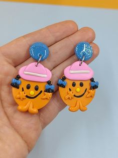 a hand holding two earrings in the shape of an orange and pink cupcake with a hat on top