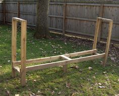 a wooden bed frame sitting in the middle of a grass covered yard next to a tree