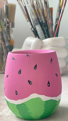 a watermelon painted cup with paintbrushes in the background