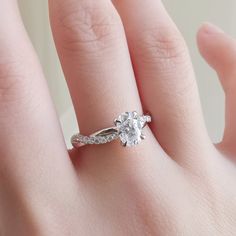 a woman's hand with a white diamond ring on her left hand and the other hand holding an engagement ring