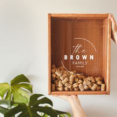 a person holding up a wooden box with wine corks in it that says the brown family