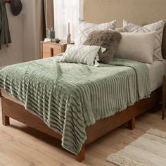 a bed with a green blanket on top of it next to a wooden night stand