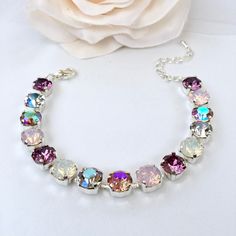 a white rose sitting next to a silver bracelet with multi colored stones on it's side