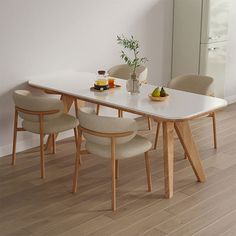 a dining table with four chairs and fruit on the plate, in front of a white wall