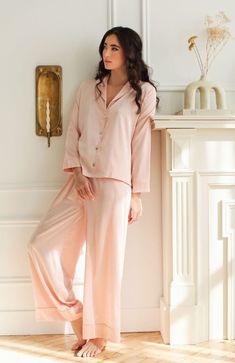 Details Let our classic charmeuse Heavenly Pajamas be your go-to 'staying-in' loungewear this season. Designed in our classic silky charmeuse fabric, these luxury pajamas feel ultra soft against the skin while giving off a lustrous sheen. Our timeless blush hue pairs perfectly with the natural look of the charmeuse fabric giving off an ethereal radiance. Mother of pearl buttons and piping detail add further touches of elegance and sophistication, while the wide-leg pajama pants do the same on th Relaxed Fit Satin Sleepwear For Loungewear, Silk Sleepwear For Pajama Party, Elegant Satin Loungewear, Elegant Silk Sleepwear For Relaxation, Elegant Satin Sleepwear For Lounging, Pink Silk Sleepwear For Loungewear, Feminine Silk Sleepwear For Loungewear, Feminine Solid Color Sleepwear For Loungewear, Elegant Relaxed Fit Sleepwear For Spring