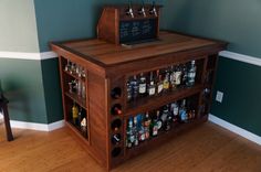 a wooden liquor cabinet with bottles and glasses on the bottom shelf next to a wall mounted chalkboard