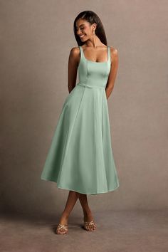 a woman in a light green dress is smiling and looking at the camera with her hands on her hips