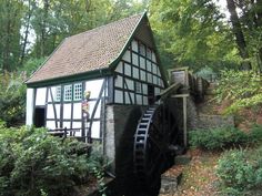 a small house with a water wheel in the middle of it's yard, surrounded by trees