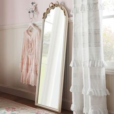 a large mirror sitting on top of a wooden floor next to a white curtain and window