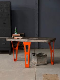 an orange table sitting on top of a cement floor next to a metal box and file cabinet