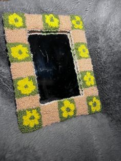 a square shaped mirror on top of a gray surface with yellow flowers in the middle