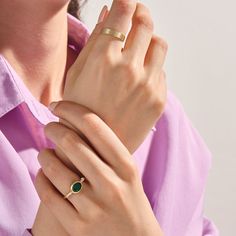 a woman wearing a gold ring with an emerald stone on her left hand and a yellow band around her wrist