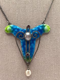 "This is a stunning antique British arts & crafts blue and green enamel, mother of pearl, and paste necklace.  The necklace is unmarked, it x-rayed as around 700 silver when tested by an XRF analyzer.  The necklace is in very good antique condition, upon close inspection, the silver swirl to the right of the mother of pearl appears to have become unsoldered from next to the mother of pearl setting, there is a tiny dot of enamel missing on the top right, a small area of enamel missing close to the mother of pearl center but mostly hidden by the mother of pearl, and there is minor enamel loss around the edges.  The necklace measures approximately 15 1/2\" long and the pendant measures approximately 2 1/8\" long by 1 3/4\" wide and weighs approximately 13.92 grams. - For international custome Vintage Blue Enamel Necklace, Unique Blue Necklace With Inlay, Collectible Blue Inlay Necklace, Art Deco Blue Pendant Necklace, Vintage Blue Necklace With Pearl Pendant, Antique Blue Cabochon Necklace, Antique Blue Pendant Necklace, Victorian Blue Pendant Necklace, Blue Victorian Pendant Necklace