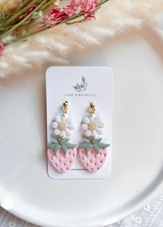 a pair of earrings with flowers on them sitting on a plate next to some pink flowers