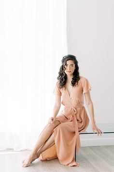 a woman is sitting on the floor in a pink dress and posing for a photo