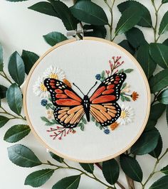 a close up of a butterfly on a embroidery hoop with flowers and leaves around it