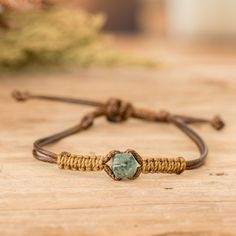 a bracelet with a green stone on it sitting on a wooden table next to a plant