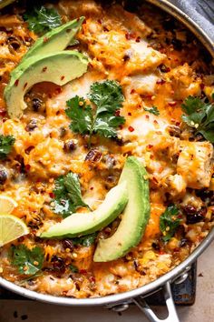 a skillet filled with chicken and rice topped with avocado, cilantro, and lime wedges