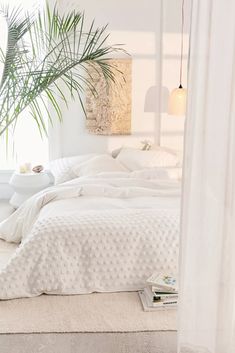 a bed with white linens and pillows in a bedroom next to a potted plant