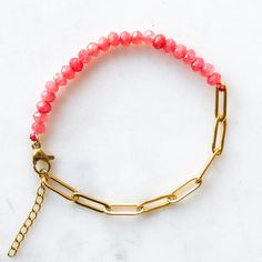 a gold chain bracelet with pink beads and a red bead on the clasp is sitting on a marble surface