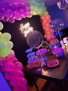 a table topped with balloons and desserts under a happy birthday sign