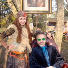 a man sitting next to a woman in front of a painting on a tree trunk