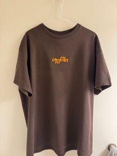 Embroidered Utopia Ambigram Logo on a brown Tshirt Shirt blank: Gildan Heavy Cotton Threading color is orange and black, shirts are made to order, special requests, including color and size, may be inquired by messaging me directly Brown Text Print Crew Neck T-shirt, Brown Crew Neck T-shirt With Text Print, Brown Short Sleeve T-shirt With Letter Print, Brown Letter Print T-shirt With Crew Neck, Brown Graphic Tee With Text Print, Brown Cotton T-shirt With Letter Print, Brown Screen Print Top For Streetwear, Brown Short Sleeve Tops With Screen Print, Brown Short Sleeve Top With Screen Print