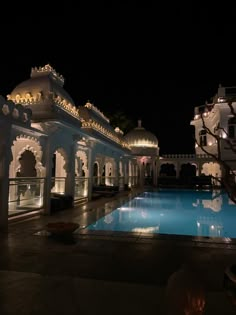 an outdoor swimming pool at night with lights on the roof and columns in the background