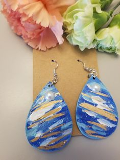 a pair of blue and gold painted tear shaped earrings next to a bouquet of flowers