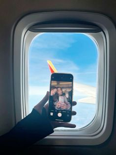 a person taking a photo on their cell phone with an airplane window in the background