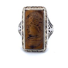 All of our jewelry is guaranteed authentic by our Graduate Gemologist of the Gemological Institute of America (GIA). 14k White Gold Filigree Genuine Natural Tiger's Eye Cameo Ring (#J4989) Art Deco 14k white gold filigree ring featuring a carved tiger's eye quartz cameo. The tiger's eye stone measures about 19.1mm x 10mm. The ring fits a size 5 3/4 finger. It weighs 3.2 dwt., and dates from the 1920's. Fantastic! Inv#RZ5350. SKU#J4989. 100% Satisfaction Guaranteed! Antique Brown Carved Jewelry, Antique Carved Sterling Silver Signet Ring, Antique Engraved Sterling Silver Ring, Antique Carved Sterling Silver Engraved Ring, Sterling Silver Intaglio Engraved Ring For Formal Occasions, Formal Sterling Silver Engraved Ring With Intaglio, Formal Sterling Silver Intaglio Engraved Ring, Antique Sterling Silver Intaglio Jewelry, Antique Filigree Ring With Cabochon For Gift