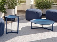 three blue tables and two round stools on the ground in front of potted plants