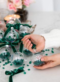 two hands are holding some glass balls with green bows on them and one hand is holding something in the other