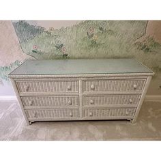 a white dresser with drawers in front of a wallpapered mural on the wall