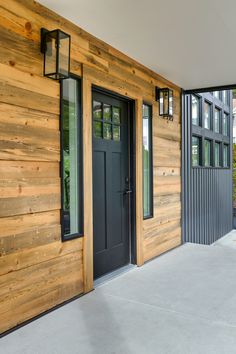 two black doors are on the side of a wooden building with windows and sidings